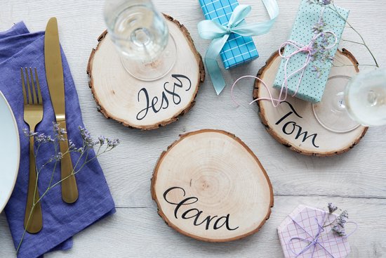 Gouden bestek en paarse servet op houten schijven met namen: Jessy, Tom, Clara. Twee geschenkdoosjes met lint.