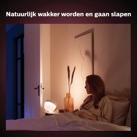 Vrouw in bed, wordt wakker door Philips Hue Iris lamp met zacht, oranje licht. Natuurlijk wakker worden en gaan slapen.