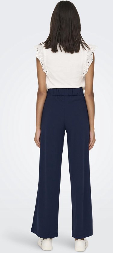 Model van achteren in een donkerblauwe broek met wijde pijpen en een witte top.
