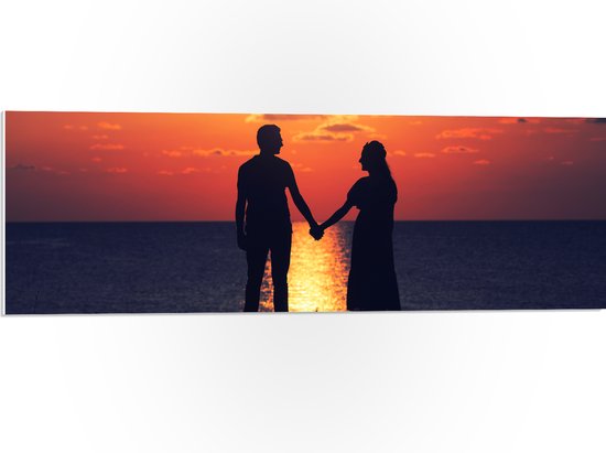 PVC Schuimplaat - Silhouet van Koppel Hand in Hand bij de Zee tijdens Zonsondergang - 90x30 cm Foto op PVC Schuimplaat (Met Ophangsysteem)