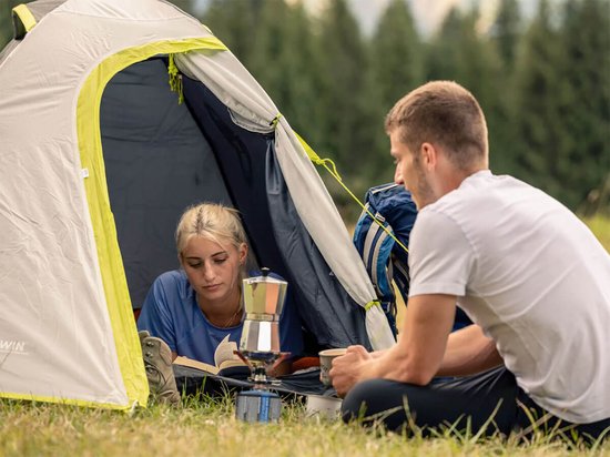 Een stel zit bij de ingang van een grijze en lichtgrijs Coleman Darwin 2 tent, met koffiezetapparaat.