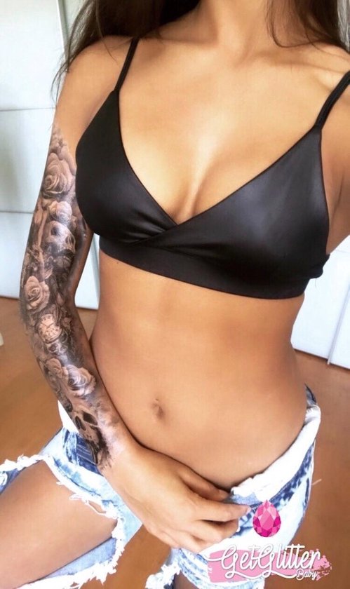 Vrouw met zwarte crop top en gescheurde spijkerbroek, met grote tatoeage op haar arm van rozen en schedels.