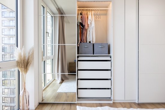 Boîtes de rangement grises dans une armoire ouverte avec des tiroirs blancs.