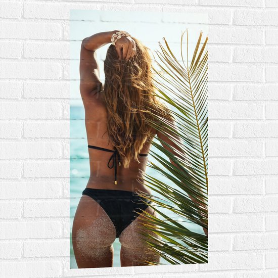 Muursticker - Achteraanzicht van Vrouw in Bikini aan Zee met Palmblad - 50x100 cm Foto op Muursticker