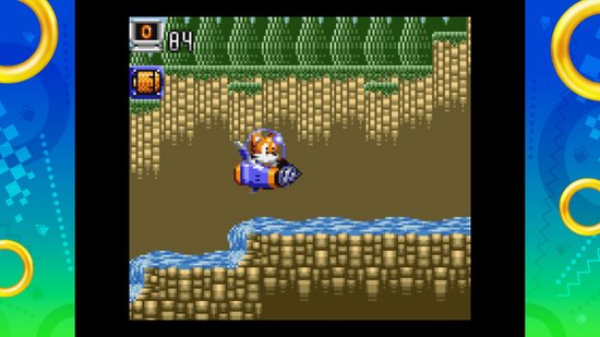 Gameplay van Sonic Origins Plus: Tails vliegt in een jetpack door een groene jungleomgeving met water.