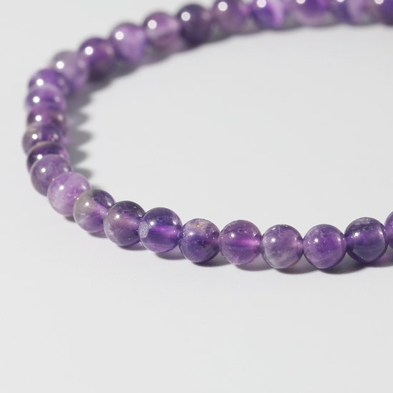Gedetailleerd beeld van een dunne armband met paarse amethistkralen.