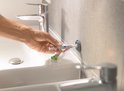 Main appliquant un adhésif avec une seringue sur une fixation murale, à côté d'un lavabo.