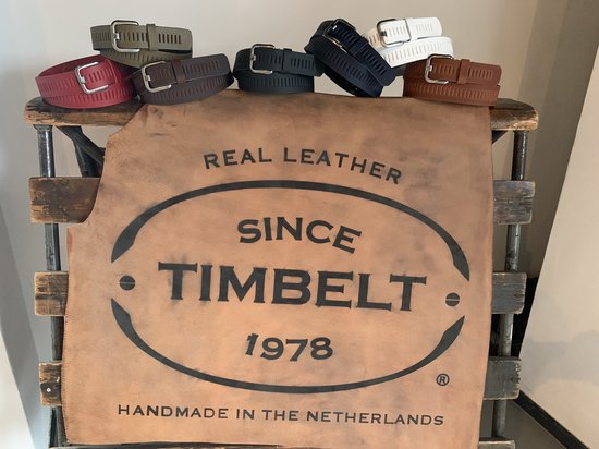 Verschillende TimBelt riemen in verschillende kleuren, waaronder rood, bruin, groen, zwart en wit, liggen op een stuk leer met TimBelt logo.
