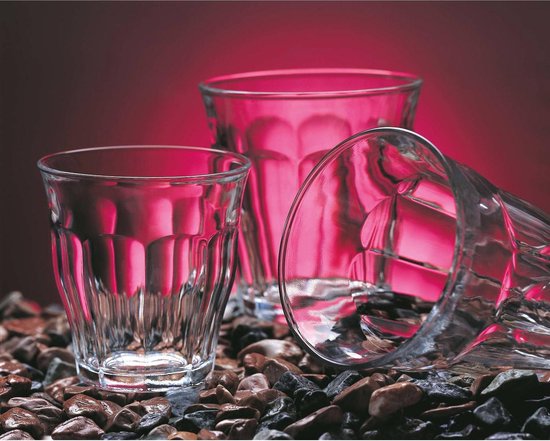 Trois verres, dont un couché, remplis de boissons rouges et bleues et posés sur des pierres.