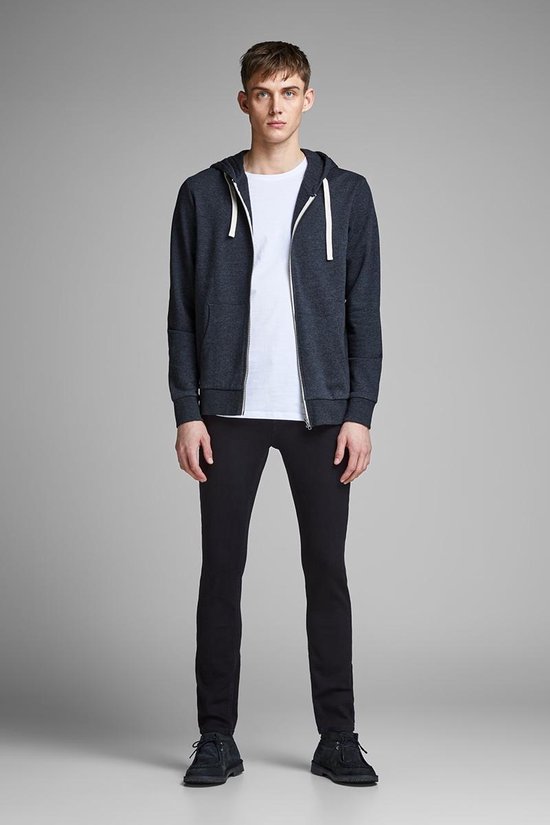 Man in zwarte skinny jeans, wit T-shirt en donkergrijs vest met rits.
