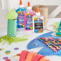 Trois bouteilles de colle Elmer's, deux à paillettes et une transparente, à côté de projets d'artisanat.