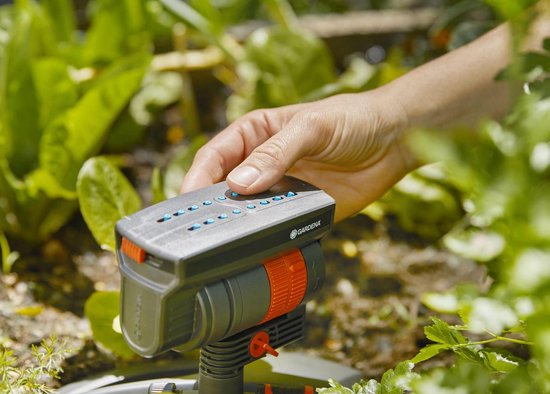 Une main utilise les boutons sur un arroseur oscillant GARDENA dans un jardin.