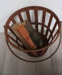 Roestbruine, metalen mand met open, rasterachtig ontwerp, handvat en gevulde houtblokken.