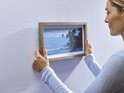 Femme accrochant un cadre photo de plage tropicale au mur.