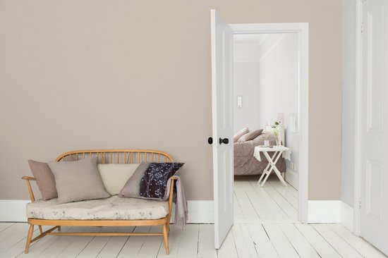 Woonkamer met houten bank, kussens en een open deur naar slaapkamer.