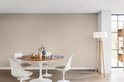 Eetkamer met ronde houten tafel, witte stoelen en een witte vloerlamp.