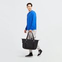 Homme en pull bleu et pantalon gris portant un sac Kipling ART M noir.