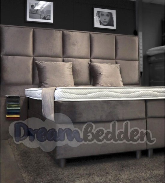 Grijze boxspring met een gestoffeerd hoofdbord, twee kussens en stofstalen.