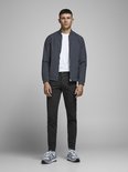 Man in donkergrijze chino broek, wit t-shirt en grijs bomberjack, gedragen met sneakers.
