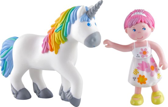 Wit speelgoed eenhoorn met regenboogmanen en staart, naast meisje met roze haar, witte jurk met bloemen, en gele schoenen.