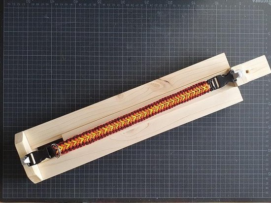 Paracord halsband in oranje, geel en rood met zwarte gesp, geweven op een knoopbord.
