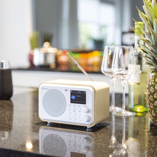 Witte retro radio met houten zijkanten op een aanrecht, met wijnglazen en ananas.