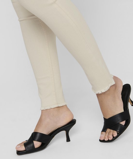 Gedetailleerde foto van crèmekleurige skinny jeans met rafelige zoom en zwarte sandalen met hak.