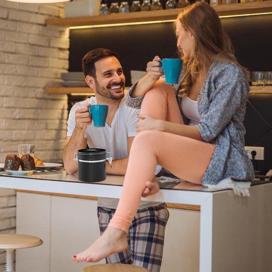Koppel in keuken die koffie drinkt. Een zwarte koffiebus staat op het aanrecht.