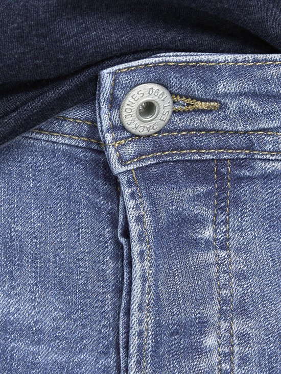 Close-up van de knoopsluiting van een blauwe spijkerbroek met tekst op de knoop.