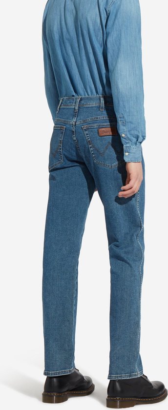 Man, staand, draagt een blauwe spijkerbroek en een denim overhemd, achterkant, met zwarte schoenen.