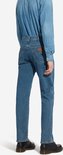 Man, staand, draagt een blauwe spijkerbroek en een denim overhemd, achterkant, met zwarte schoenen.