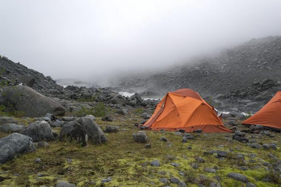Oranje tent met een rivier en rotsachtig terrein op de achtergrond.