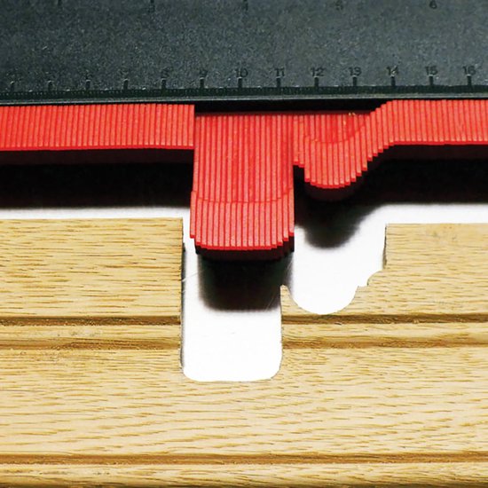 Rode contourmal met zwarte schaalverdeling, die een profiel op houten planken aftekent.