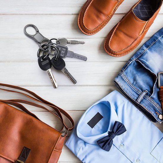 Zwarte karabijnhaak sleutelhanger met sleutelbos, naast bruine herenschoenen, jeans, overhemd en tas.