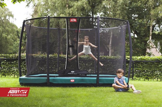 Meisje springt op trampoline met veiligheidsnet, jongen zit op gras.