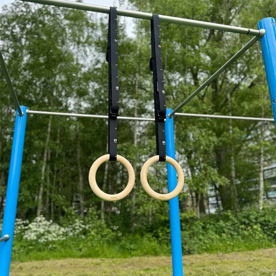 KRAKEN gymringen van hout met zwarte, verstelbare SafeLock ophangbanden aan een rek.