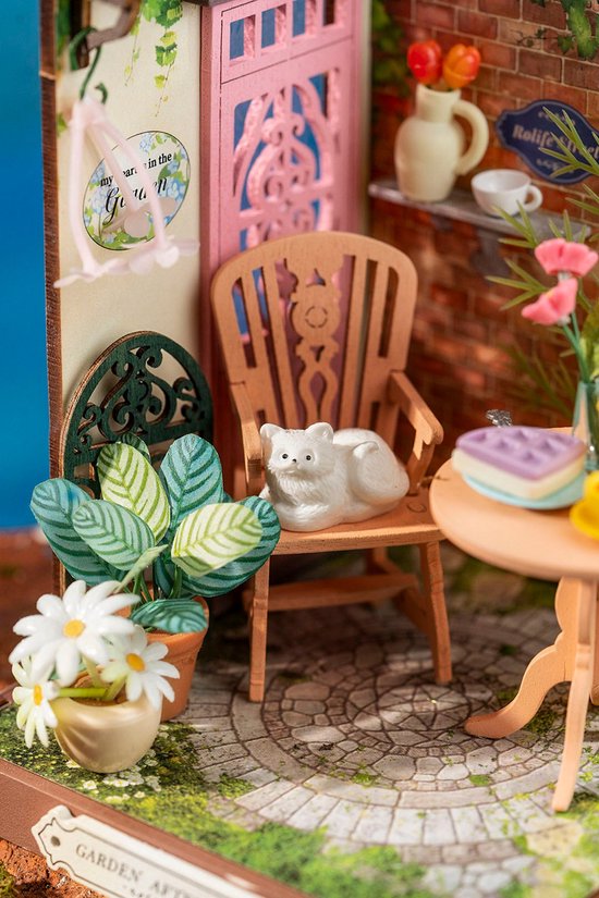 Close-up van een miniatuur stoel met een wit katje, naast een plant met witte bloemen.