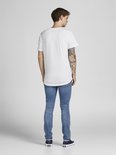 Een man met tatoeages op zijn arm draagt een witte t-shirt met korte mouwen en een ronde hals, van achteren gezien, gecombineerd met een spijkerbroek.