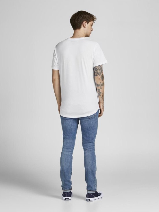 Een man met tatoeages op zijn arm draagt een witte t-shirt met korte mouwen en een ronde hals, van achteren gezien, gecombineerd met een spijkerbroek.