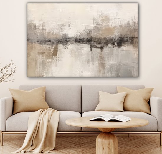 Tableau abstrait dans des tons beige, gris et brun, accroché au-dessus d'un canapé avec des coussins et une table d'appoint avec un livre.