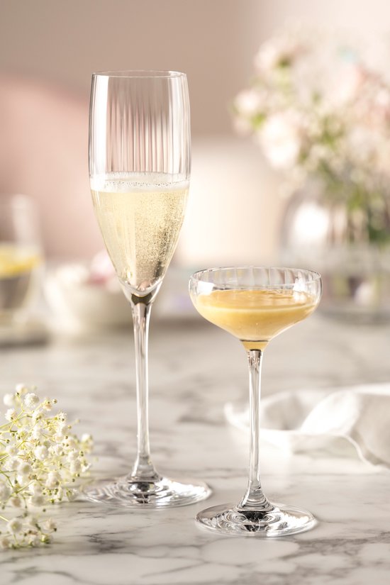 Twee champagneglazen met verticale ribbels, één gevuld met champagne, de ander met een gele vloeistof.