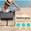 Een vrouw met strooien hoed op het strand leunt achterover in een grijze strandmat met opbergvak. Tekst: Handige opbergtas.