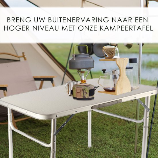 Zilverkleurige campingtafel met kampeerspullen zoals een brander, mokken en een waterkoker, in een buitenomgeving.