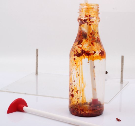 Een witte flessenschraper met rood uiteinde in een fles met chilisaus.