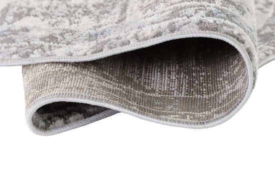 Vue détaillée du dessous et du bord d'un tapis rond gris enroulé avec un motif subtil.