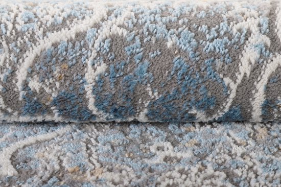 Gros plan d'un tapis rond gris à texture usée, avec des détails de fils bleus et blancs formant le motif.