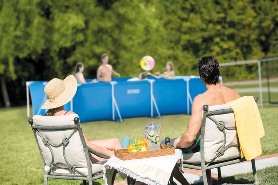 Koppel kijkt naar een blauw Intex zwembad waar mensen in spelen, zittend in tuin.