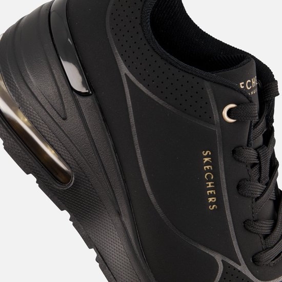 Detail van een zwarte Skechers sneaker met goudkleurige merknaam en veters.