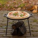 Pizza met ham, tomaatjes en kruiden op een pizzasteen op een metalen standaard.