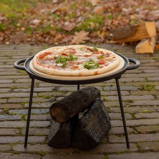 Pizza met ham, tomaatjes en kruiden op een pizzasteen op een metalen standaard.